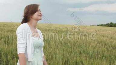 美丽的少女，在田野里高高的绿色小麦穗中。 年轻快乐的女人享受夏天，人与人的和谐